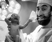 A new born baby is trying to remove the doctors mask who was holding the baby. from new born baby dilivery